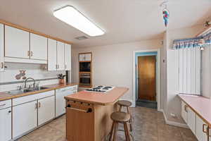 Kitchen featuring sink, a breakfast bar area, white cabinetry, a center island, and white appliances