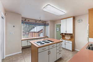 Kitchen with light tile patterned flooring, sink, white electric cooktop, a kitchen island, and white cabinets