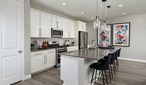 Kitchen with pendant lighting, sink, appliances with stainless steel finishes, white cabinetry, and a center island with sink