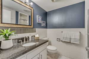 Bathroom featuring tile patterned flooring, vanity, tile walls, and toilet