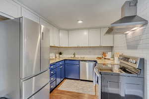 Kitchen featuring blue cabinets, light stone counters, island range hood, appliances with stainless steel finishes, and white cabinets