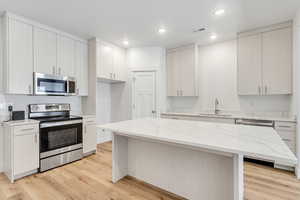 Kitchen with appliances with stainless steel finishes, sink, white cabinets, a center island, and light hardwood / wood-style flooring