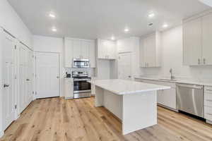 Kitchen with appliances with stainless steel finishes, a center island, light stone counters, white cabinets, and light wood-type flooring