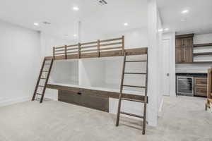 Unfurnished bedroom featuring wine cooler, light colored carpet, and bar area