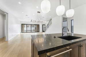 Kitchen featuring a kitchen island with sink, sink, hanging light fixtures, and dark stone countertops