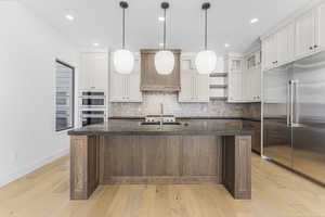 Kitchen featuring stainless steel appliances, a kitchen island with sink, sink, and white cabinets