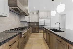 Kitchen with premium range hood, decorative light fixtures, white cabinetry, sink, and stainless steel appliances