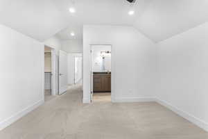 Interior space with light carpet, ensuite bath, a walk in closet, and vaulted ceiling