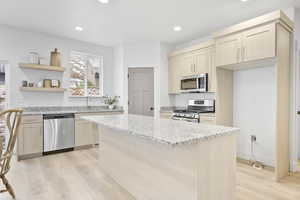 Kitchen with appliances with stainless steel finishes, sink, a center island, light hardwood / wood-style floors, and light stone countertops