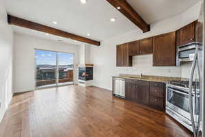 Kitchen featuring appliances with stainless steel finishes, beamed ceiling, sink, light stone countertops, and dark wood-type flooring