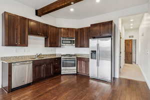 Kitchen featuring sink, dark wood-type flooring, beam ceiling, stainless steel appliances, and light stone counters