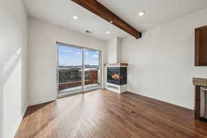 Unfurnished living room featuring a multi sided fireplace, dark hardwood / wood-style flooring, and beam ceiling