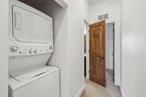 Laundry room with stacked washing maching and dryer and light carpet