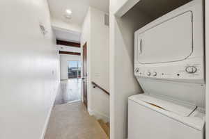 Clothes washing area featuring stacked washer and dryer and light colored carpet