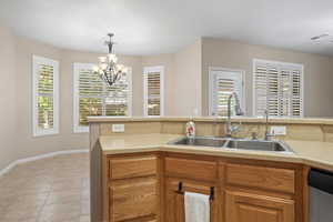 Kitchen with dishwasher, sink, hanging light fixtures, light tile patterned floors, and an inviting chandelier