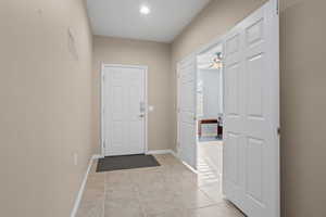 Doorway with light tile patterned floors and ceiling fan