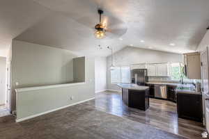 Kitchen featuring lofted ceiling, white cabinetry, hanging light fixtures, a kitchen island, and stainless steel appliances