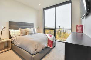 Bedroom featuring light colored carpet and a wall of windows