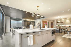 Kitchen featuring stainless steel oven, sink, decorative light fixtures, and an island with sink