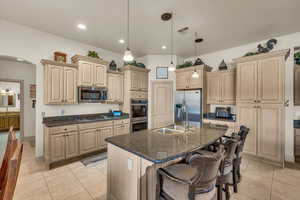 Kitchen with sink, decorative light fixtures, dark stone countertops, appliances with stainless steel finishes, and a kitchen island with sink