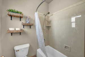 Bathroom with toilet and shower / bathtub combination with curtain