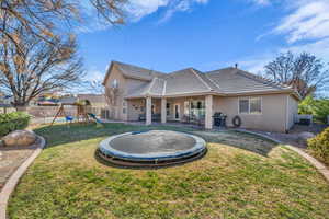 Back of house with ceiling fan, a yard, a playground, and a trampoline