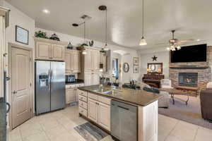 Kitchen with appliances with stainless steel finishes, a fireplace, an island with sink, sink, and hanging light fixtures