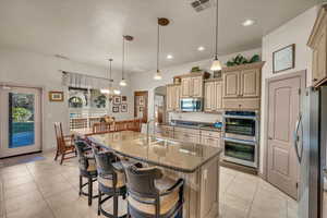 Kitchen featuring sink, decorative light fixtures, dark stone countertops, stainless steel appliances, and a kitchen island with sink