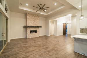 Unfurnished living room with a fireplace, dark hardwood / wood-style flooring, ceiling fan, a tray ceiling, and a barn door