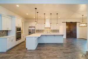 Kitchen featuring hanging light fixtures, premium range hood, a barn door, and appliances with stainless steel finishes