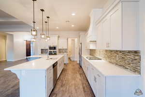 Kitchen featuring sink, appliances with stainless steel finishes, a spacious island, white cabinets, and decorative light fixtures