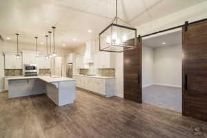 Kitchen featuring white cabinetry, hanging light fixtures, stainless steel appliances, and a barn door