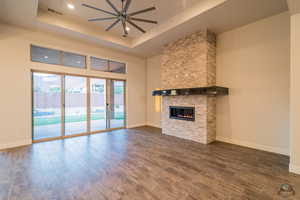 Unfurnished living room featuring a tray ceiling, dark hardwood / wood-style floors, a towering ceiling, ceiling fan, and a fireplace