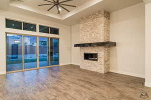 Unfurnished living room featuring ceiling fan, wood-type flooring, a fireplace, and a tray ceiling