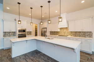 Kitchen with white cabinetry, appliances with stainless steel finishes, and a large island with sink