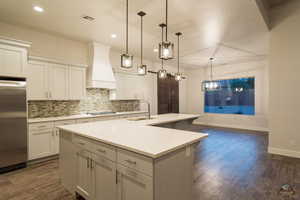 Kitchen with sink, appliances with stainless steel finishes, custom range hood, pendant lighting, and a kitchen island with sink