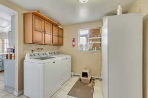 Clothes washing area featuring cabinets, light tile patterned flooring, washer and dryer, and a wealth of natural light