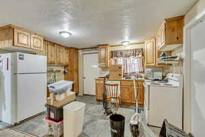 Kitchen with light brown cabinetry, white appliances, and a textured ceiling