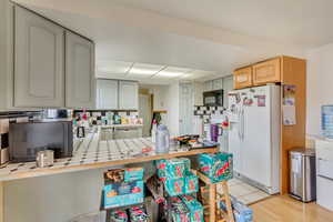 Kitchen with white appliances, tile countertops, kitchen peninsula, and decorative backsplash