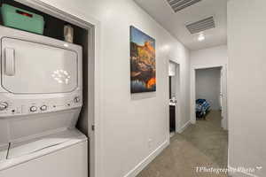 Washroom featuring stacked washer and dryer and light carpet