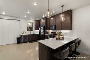 Kitchen with stainless steel appliances, kitchen peninsula, dark brown cabinetry, and decorative light fixtures