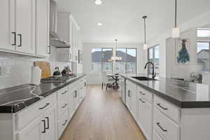 Kitchen featuring sink, hanging light fixtures, stainless steel appliances, a large island with sink, and wall chimney exhaust hood