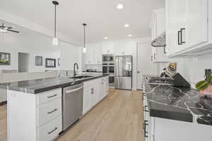 Kitchen featuring a kitchen island with sink, sink, stainless steel appliances, and white cabinets