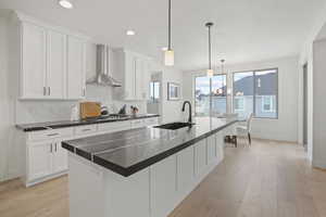Kitchen with a kitchen island with sink, sink, white cabinets, and wall chimney exhaust hood
