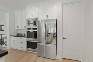 Kitchen with an inviting chandelier, light hardwood / wood-style floors, white cabinets, and appliances with stainless steel finishes