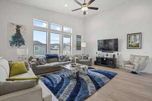 Living room featuring ceiling fan, hardwood / wood-style floors, and a towering ceiling