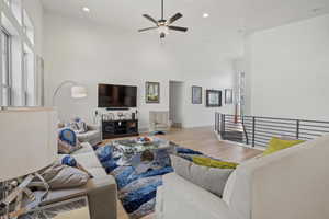 Living room with ceiling fan, a towering ceiling, and light hardwood / wood-style floors