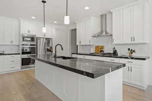 Kitchen with wall chimney exhaust hood, sink, hanging light fixtures, a center island with sink, and appliances with stainless steel finishes