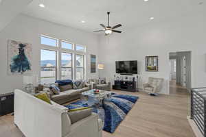 Living room with light hardwood / wood-style flooring, ceiling fan, and a high ceiling