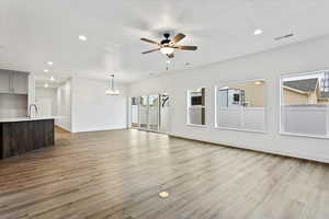 Unfurnished living room with sink, ceiling fan with notable chandelier, a textured ceiling, and light wood-type flooring